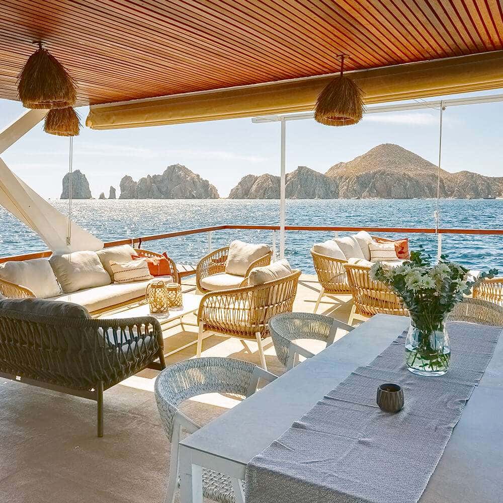 Covered deck lounge with woven sofas, armchairs and a dining table, rocks beyond