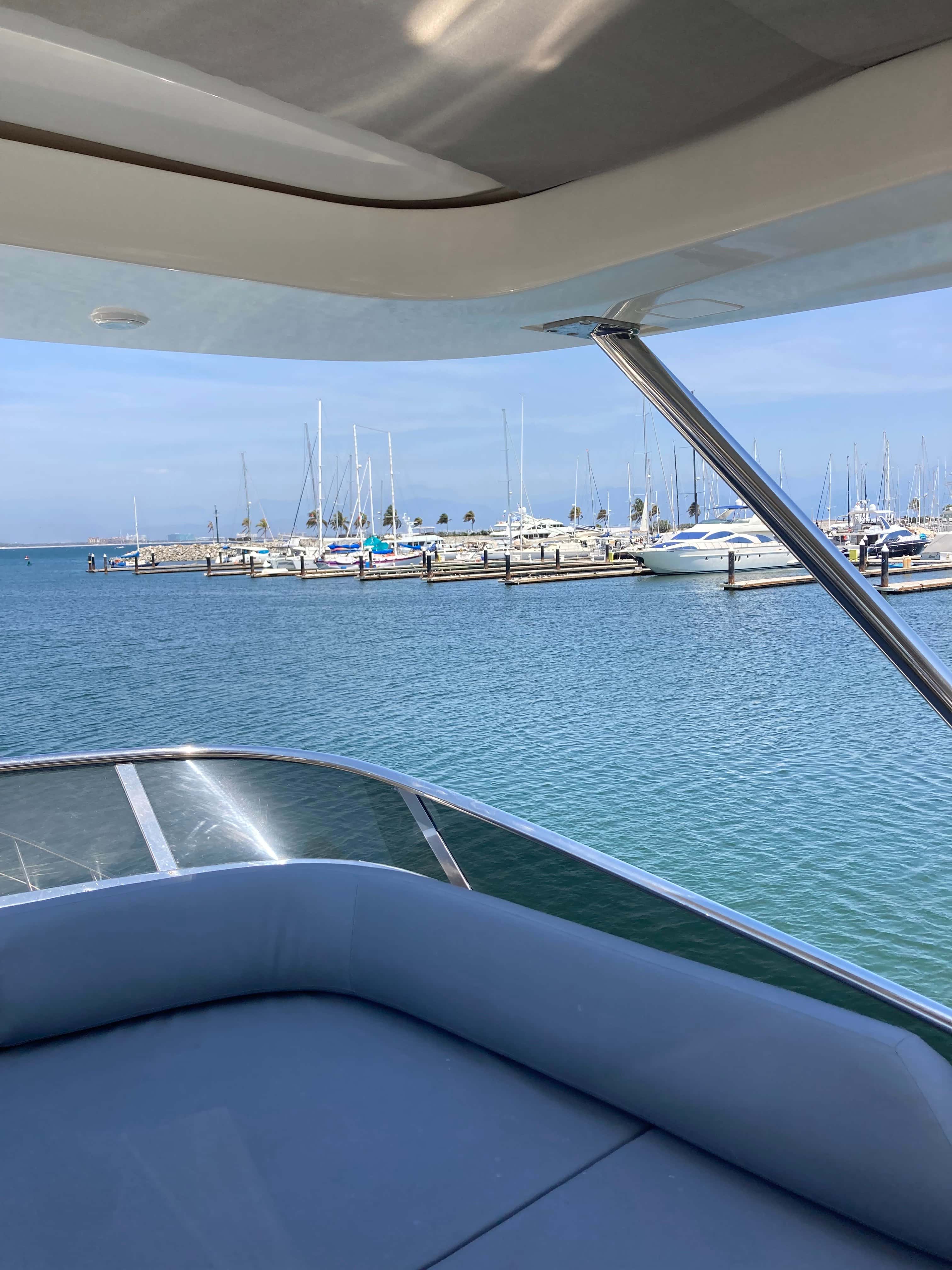 Cushioned flybridge seating under the hardtop, looking over the marina and moored boats